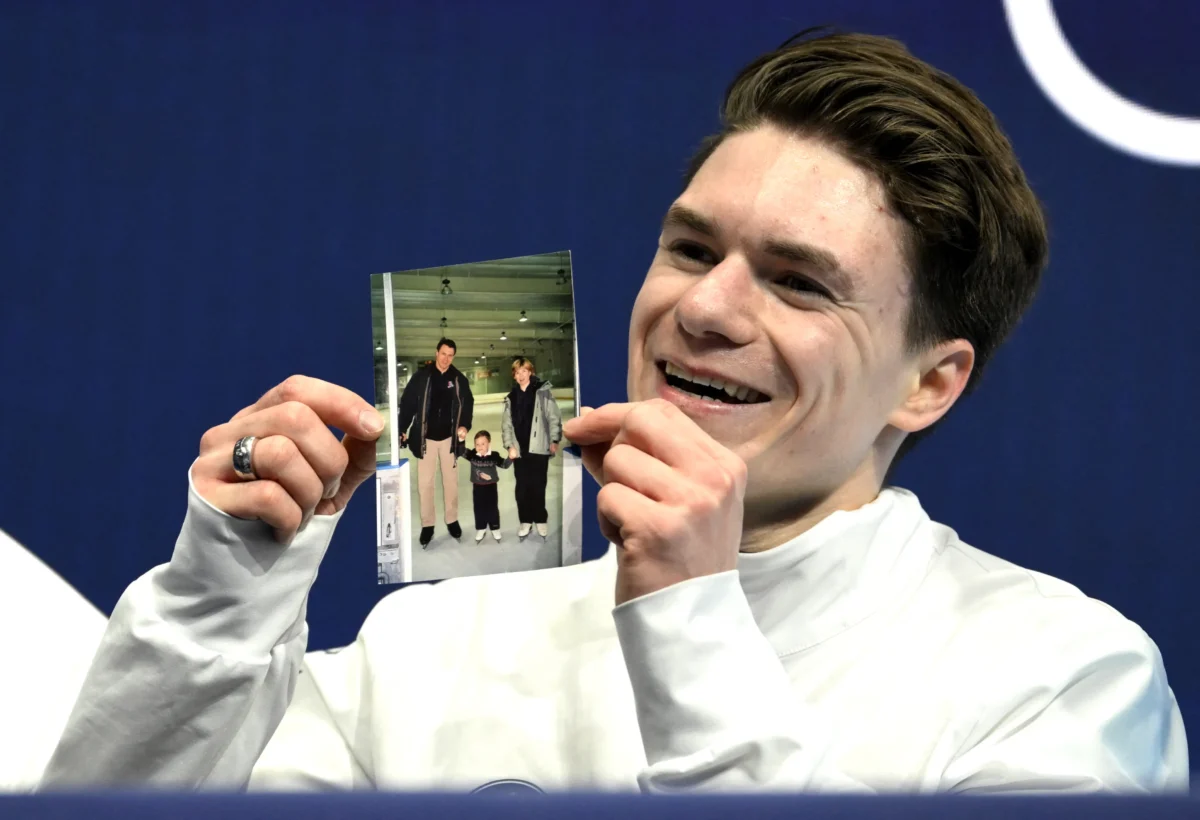 Maxim Naumov of the United States holds a picture of his parents, who died in a plane crash last year, after competing in the figure skating men's singles short program during the Milano Cortina 2026 Winter Olympic Games at Milano Ice Skating Arena in Milan on Feb. 10, 2026. (Wang Zhao/AFP via Getty Images)
