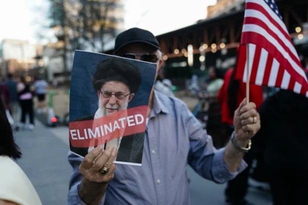 A man in Atlanta, Ga., holds a U.S. flag and a sign with a portrait of the Iranian leader Ayatollah Ali Khamenei who was killed during U.S.–Israel military operations against the Islamic Republic, on Feb. 28, 2026. (Elijah Nouvelage/AFP via Getty Images)