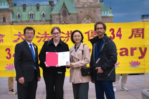 Falun Dafa Association of Canada representatives stand alongside an assistant of Liberal MP Amandeep Sodhi holding a proclamation from the MP marking World Falun Dafa Day, on Parliament Hill in Ottawa on May 5, 2026. (Evan Ning/The Epoch Times)