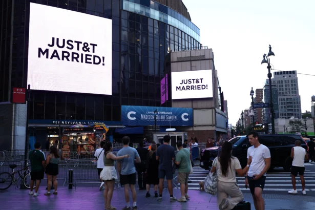 People watch giant screens showing the message "JUST&T MARRIED!" (T&T for Taylor and Travis) outside Madison Square Garden, the reported venue for the wedding celebrations of pop singer Taylor Swift and pro-athlete Travis Kelce, in New York City on July 3, 2026. (Charly Triballeau/AFP via Getty Images)