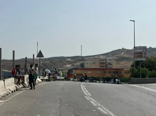 Young illegal immigrants gather near road signs pointing toward Príncipe Alfonso and El Tarajal in Ceuta, Spain, on Aug. 1, 2026. Several told The Epoch Times they planned to stay in the Spanish enclave. (Etienne Fauchaire/The Epoch Times)