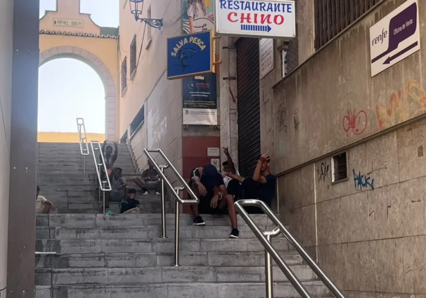 Moroccan illegal immigrants sit on the steps near the Rafael Gibert archway in Ceuta, Spain, on Aug. 1, 2026. (Etienne Fauchaire/The Epoch Times)