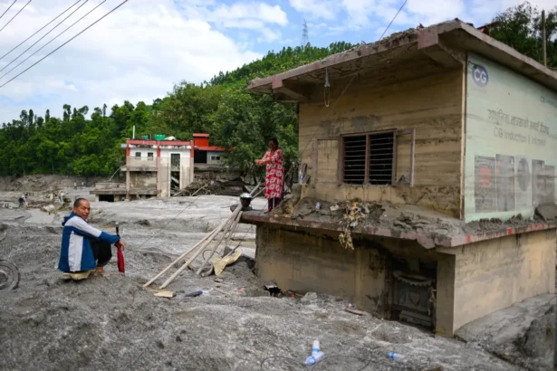 A woman (R) stands atop her house covered in mud in the aftermath of flash floods at Baireni in Nepal's Dhading district on Aug. 30, 2026. (Manan Vatsyayana/AFP via Getty Images)
