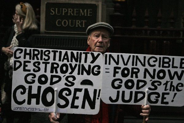 Protester Joe Mitchell, 83, holds banners against the church as he drove more than 1,000 kilometers (600 miles) from his home in Newcastle, New South Wales state, to the Victoria state Court of Appeal in Melbourne, Australia, on June 5, 2019. (AP Photo/Rod McGuirk)