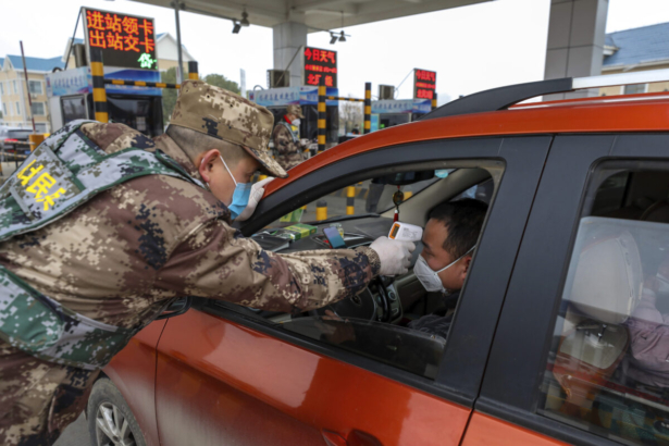 A militia member uses a digital thermometer to take a driver's temperature at a checkpoint at a highway toll gate in Wuhan in central China's Hubei Province on Jan. 23, 2020. (Chinatopix via AP)