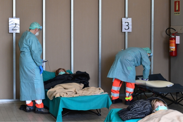 Hospital employees wearing masks and gear tend to patients lying in bed at a temporary emergency structure set up outside the accident and emergency department, where any new arrivals presenting suspect new coronavirus symptoms will be tested, at the Brescia hospital, Lombardy, Italy, on March 13, 2020. (Miguel Medina/AFP via Getty Images)