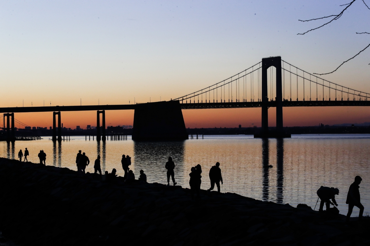 People gather to watch the sun set behind the Throgs Neck Bridge at LIttle Bay Park in the Queens borough of New York City on April 8, 2020. (Frank Franklin II/AP Photo)