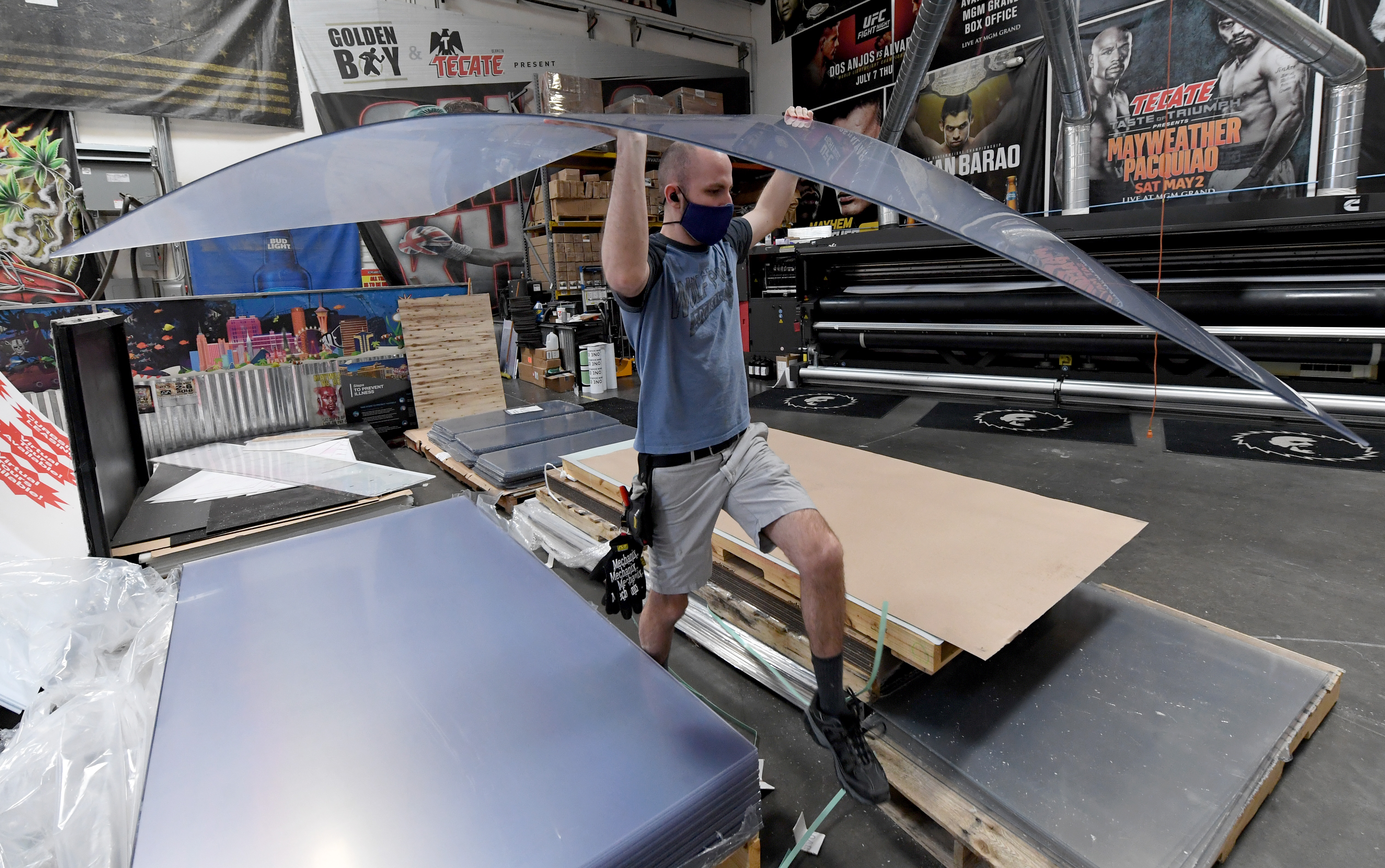 Jaeden Milam carries a sheet of acrylic to a computer-controlled cutting machine as he makes safety shield dividers at Screaming Images amid the spread of the coronavirus in Las Vegas, Nev., on May 18, 2020. (Ethan Miller/Getty Images)