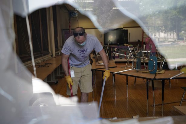 Jake Loewen is seen cleaning up through a broken window at the Harborside Academy in Kenosha, Wis., on Aug. 24, 2020. (Morry Gash/AP Photo)