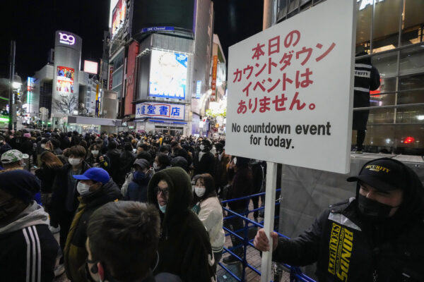 A security guard holds up a sign indicating that there is no countdown event at the famed Shibuya scramble crossing, a popular location for a New Year’s Eve gathering, in Tokyo as people gather to celebrate New Year’s eve on Dec. 31, 2021. (Kiichiro Sato/AP Photo)