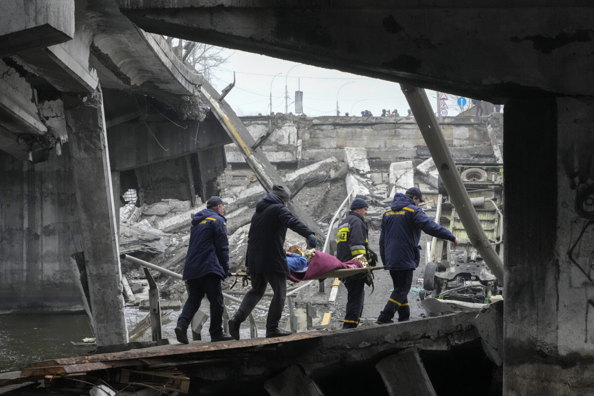 Ukrainian rescue workers carry an elderly woman under the destroyed bridge in Irpin, near Kyiv, Ukraine, on April 1, 2022. (Efrem Lukatsky/AP Photo)